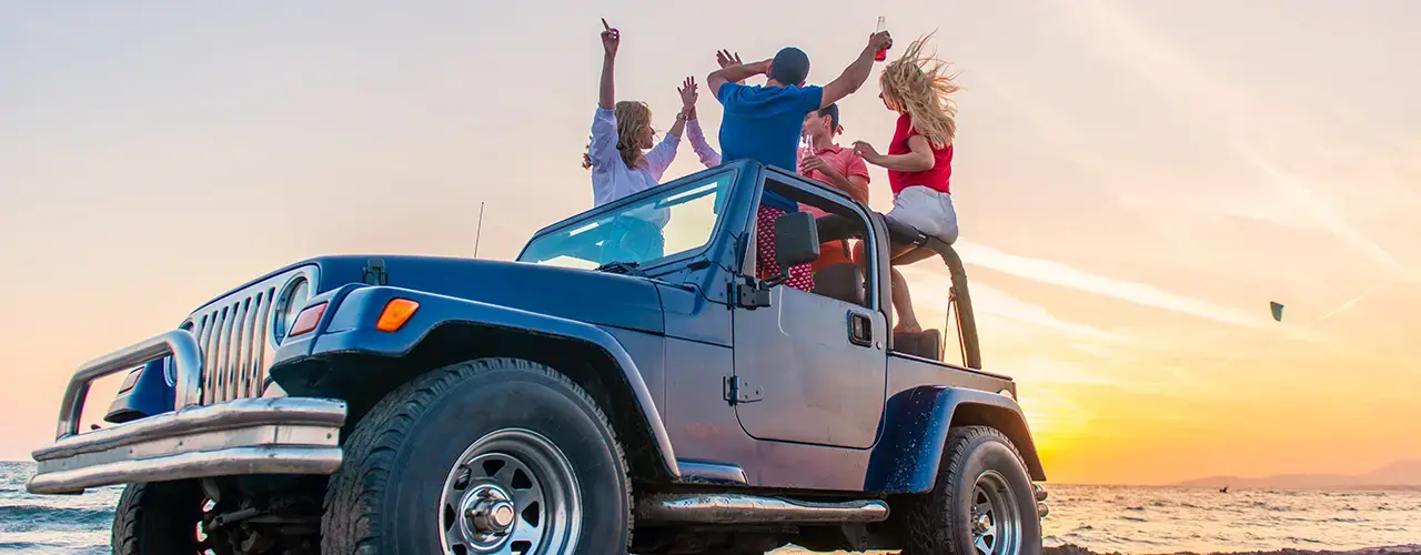 A group of friends joyfully riding atop a jeep, enjoying an adventurous outdoor experience