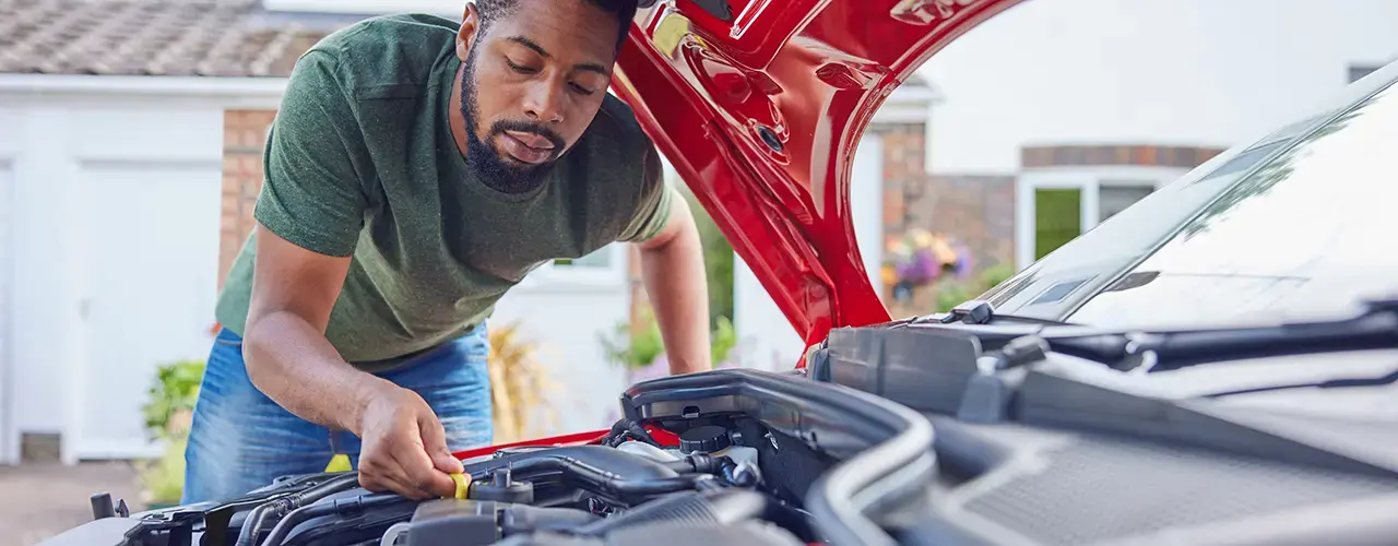 A man inspects the engine compartment of his car under a bonnet