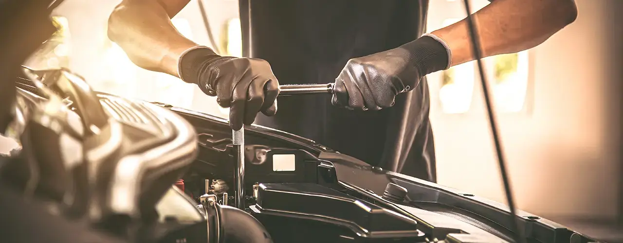 A man wearing black gloves is focused on repairing a car under bonnet